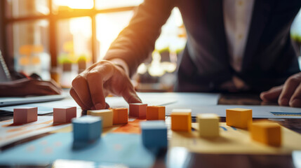 Business strategy meeting with hand arranging colored blocks on a table in a sunlit office. Concept of planning and teamwork.