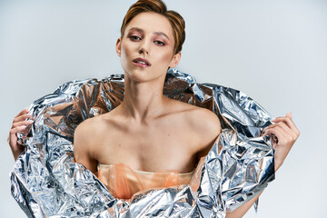 A woman in a silver foil garment, posing with a confident and alluring gaze.