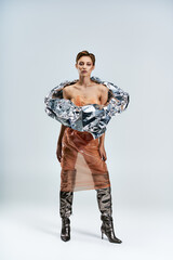 A woman poses in a studio, wearing a silver foil top and a plastic skirt.
