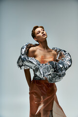 A woman poses in a studio, wearing a silver and orange ensemble crafted from sustainable materials.