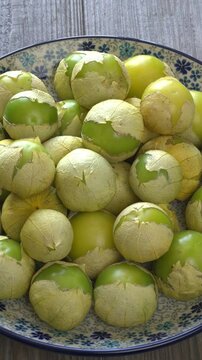 A pile of ripe tomatillo on a hand-colored plate. Table spin. Vertical video.