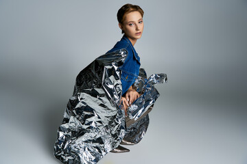 A woman sits, wrapped in a silver blanket, a blue denim jacket framing her thoughtful expression.