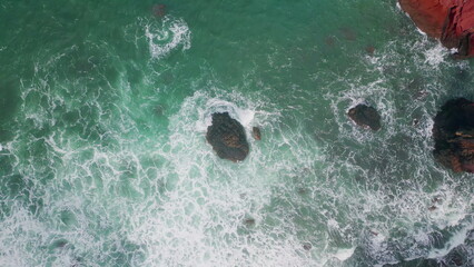 Top turquoise sea splashing rocks. Drone view of powerful ocean water washing