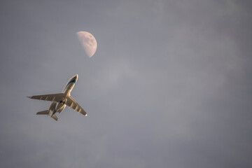 Commercial jet airliner flying below half moon