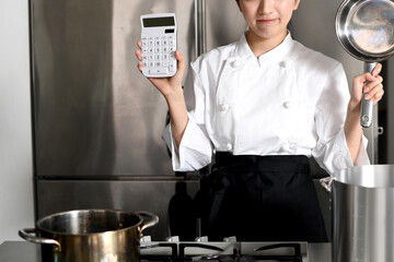 鍋と電卓を持ち悩むアジア人の女性調理師