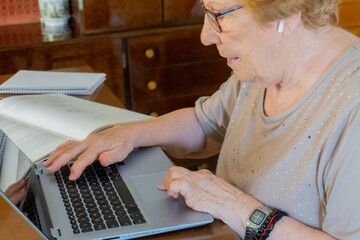 Elderly woman at home studying with a laptop and a book
