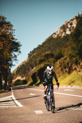 A woman cyclist training on a lonely road on a sunny day wearing a black jersey and bib shorts and...