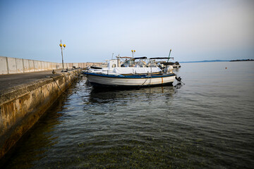 Small fishing boat with outboard motor moored to a concrete pier on calm water