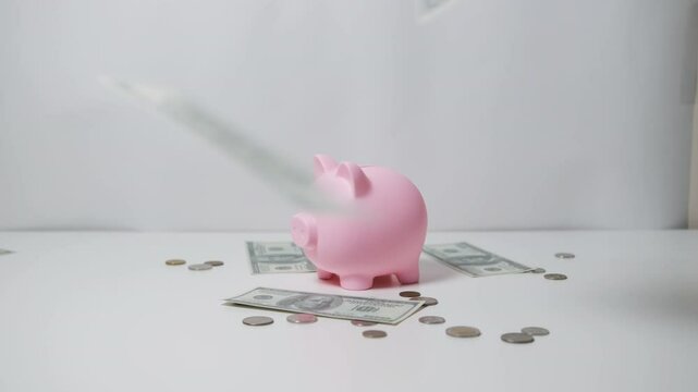 Money bills fall on the pink piggy bank and the table where the coins are scattered. Financial prosperity and success