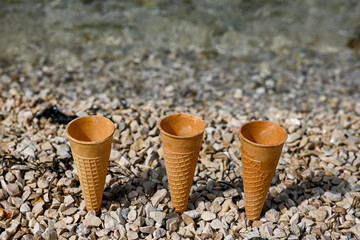 Enjoying summer vibes with empty ice cream waffle cones on a pebble beach, with the sparkling sea as a backdrop