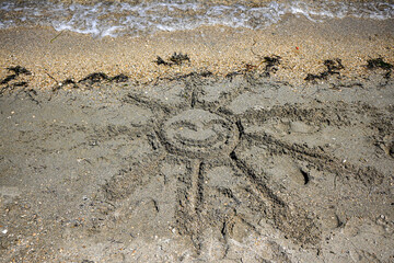 Sun drawing in the sand on a beach with ocean waves crashing on shore
