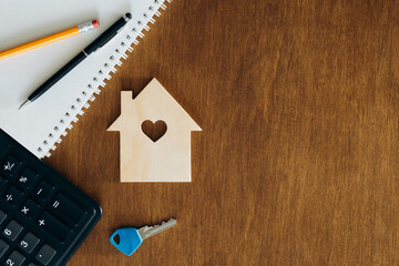 Wooden house model, calculator and key on a wooden table, flat lay.