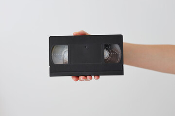A person is holding a black VHS tape. The tape is black and white and has a checkered pattern
