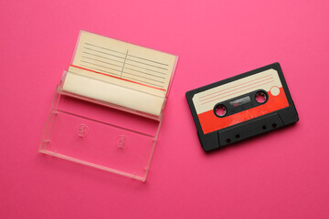 A cassette tape is sitting on a pink background. The tape is red and white
