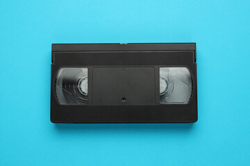 A black VHS tape is laying on a blue background. The tape is empty and has no visible content