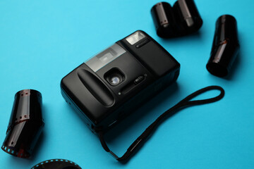 A black camera sits on a blue surface with a bunch of film rolls. The camera is surrounded by the film rolls, which are all different sizes and colors