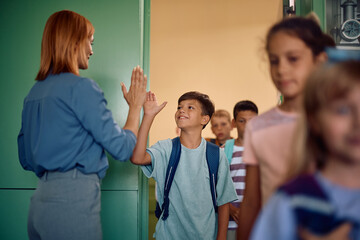 Happy school kids greeting their teacher while entering in  classroom.