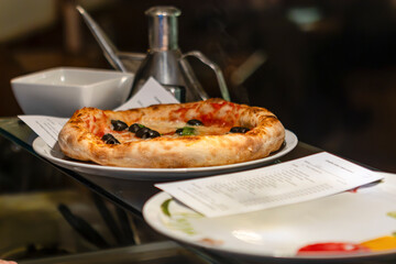 Freshly baked pizza with olives and basil oil on display