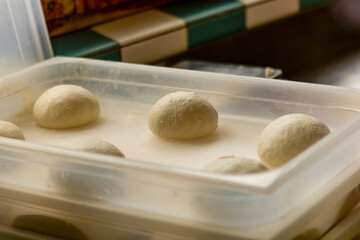 Fresh pizza dough balls rising in a tray