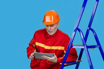 Serious senior male factory or construction worker using a digital tablet. Isolated on blue.