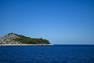 Fototapeta premium Small rocky island emerging from the deep blue sea on sunny summer day
