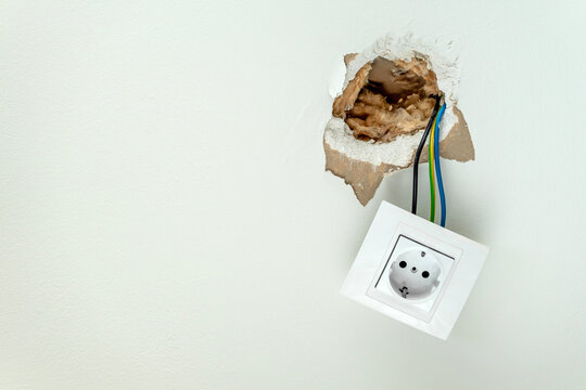 Damaged electrical socket hanging from wall. Home insurance for emergency failures repairs. Copy space.