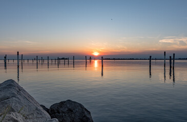 Obraz premium Serene Sunset on the Sea in Grado: Splendid Reflections and Colors Admired from a Rocky Pier.