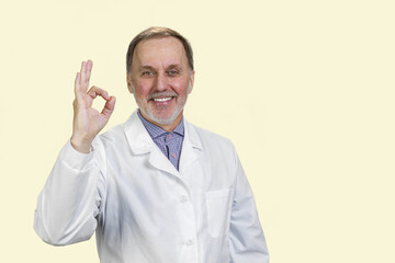 Happy male senior medic in white coat shows okay gesture sign. Isolated on white.