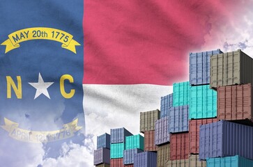 North Carolina US state flag and big stack of shipping cargo containers in docks with sky background close up