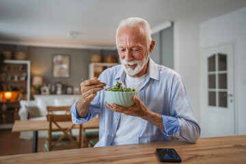 Portrait of senior man stand at home and eat salad