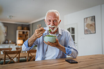 Portrait of senior man stand at home and eat salad