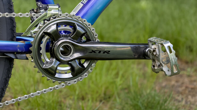 Top of the line 11 speed double Shimano XTR M9000 crankset on a blue mountain bike with SPD pedals with green grassy lawn background.
