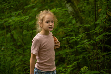 A young girl wearing a pink shirt explores a lush forest, clutching a toy. Her expression is one of curiosity and focus as she navigates through the greenery.