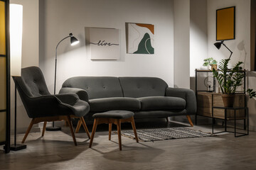 Grey sofa, armchair and stool in interior of living room at night