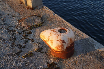 Obraz premium Close up of old rusted peach mooring bollard on the stone pier.. Navy sea water. Noblessner, Tallinn, Estonia. July 2024