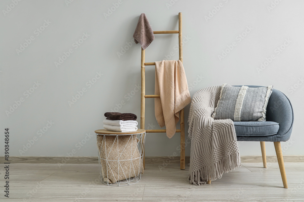 Poster Stack of clean soft towels on table, armchair and stepladder near white wall in room