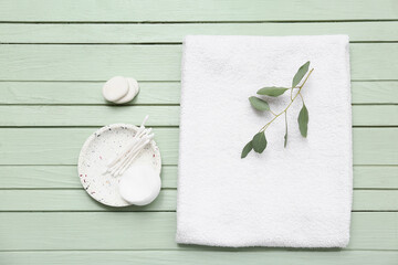 Clean soft towel, marble plate, spa stones, cotton pads and buds on green wooden background