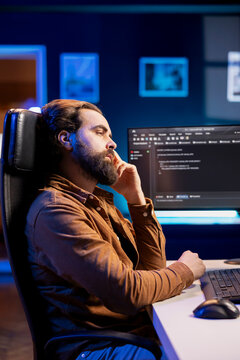 Bored programmer fixing vulnerabilities in software enabling hackers to compromise systems, waiting for shift to end. Impassive man wearied by job, using PC to patch security exposures