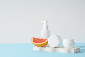 Composition with grapefruit, plaster stand, jars of cream and bottle of lotion on blue background