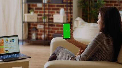 Remote worker looking at isolated screen cellphone while optimizing market performance charts. Indian woman checking online business analytics statistical data metrics on chroma key phone and laptop