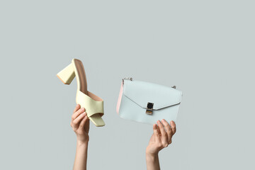 Female hands with bag and heeled shoe on grey background