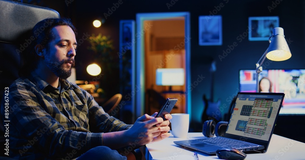 Poster man taking break from checking financial graphs on laptop, playing games on phone. remote worker rel