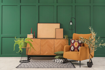 Cozy armchair with cushion, chest of drawers with frames and decorative olive tree in interior of...
