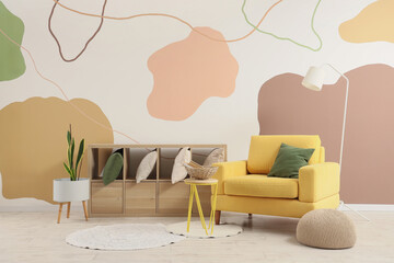 Cozy armchair, lamp and shelving unit with cushions in interior of living room