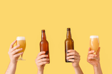 Hands holding beer glasses and bottles on yellow background