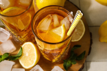 Glasses of tasty cold ice tea, wooden tray and lemons on tile background, closeup