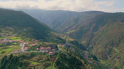 Fototapeta premium Small town surrounded mountain hills drone view. Village nestled in green valley