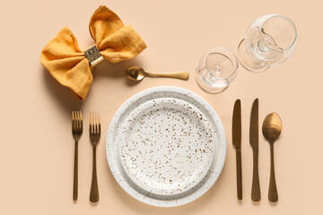 Beautiful table setting with golden cutlery and yellow napkin on beige background