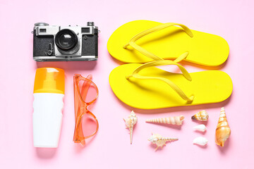 Flip-flops, photo camera, sunglasses, bottle of sunscreen and seashells on pink background