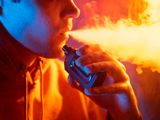 Vaper exhales the vapor of an electronic cigarette, close-up. Colored light